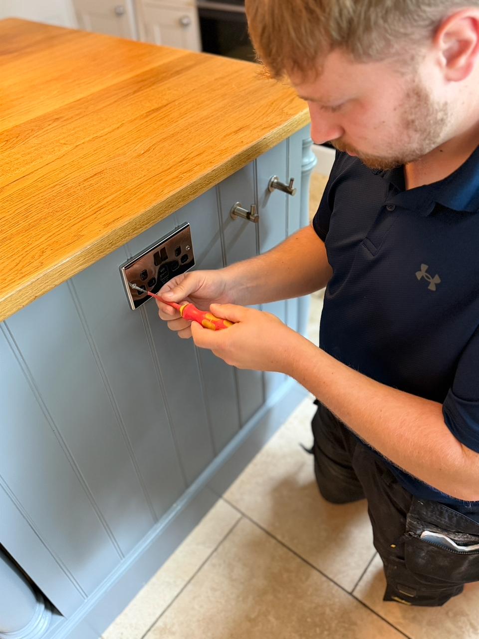 Ollie kneeling and using a screwdriver on a chrome double socket in a kitchen island