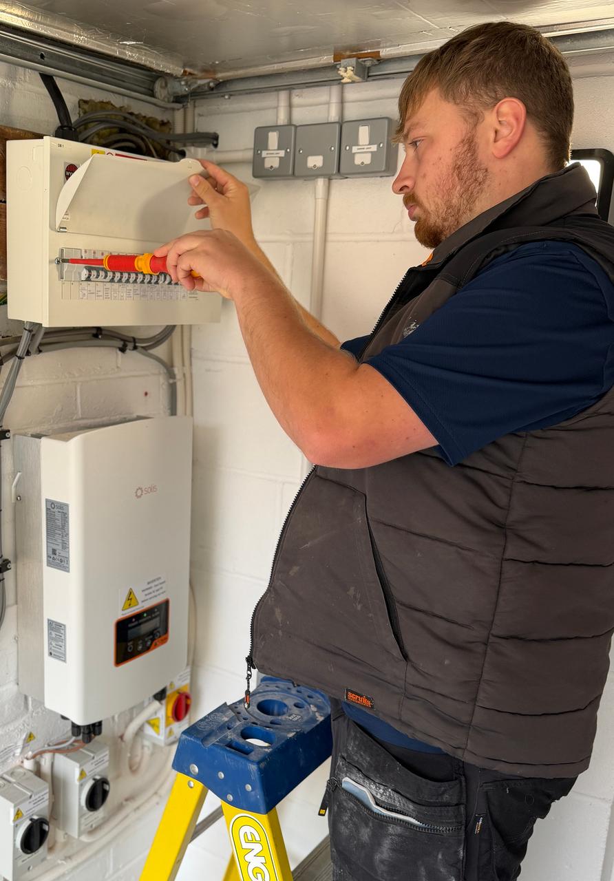 Ollie on a ladder using an insulated screwdriver on a circuit breaker in an open fuse box